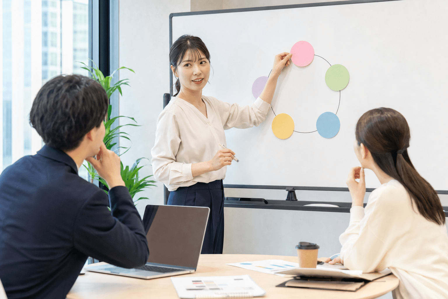 ホワイトボードに5つの円を並べて説明する人事企画担当者