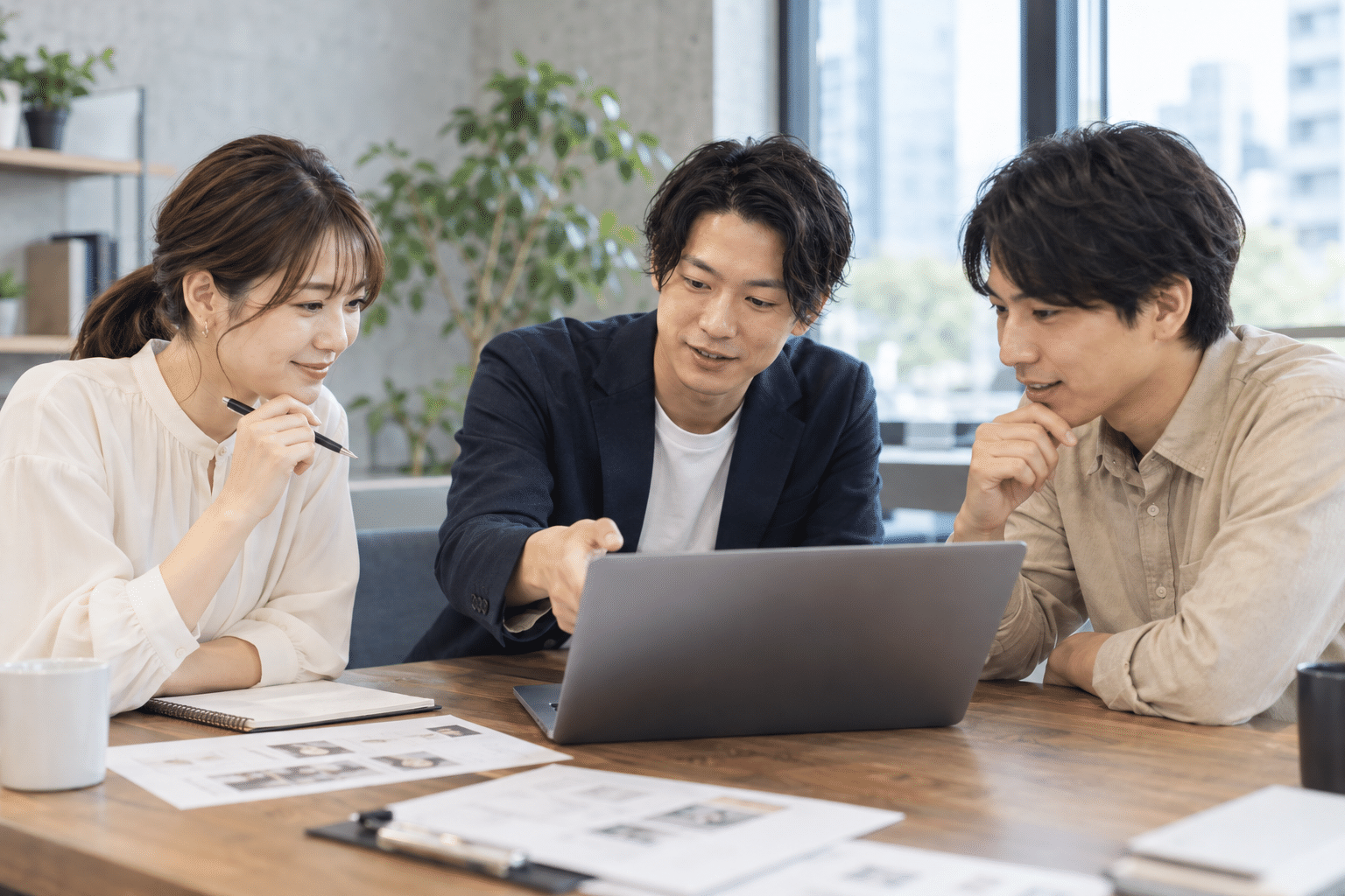 日本人の男女3人がPCの動作を確認し、紙のチェックリストを机に置いて話す