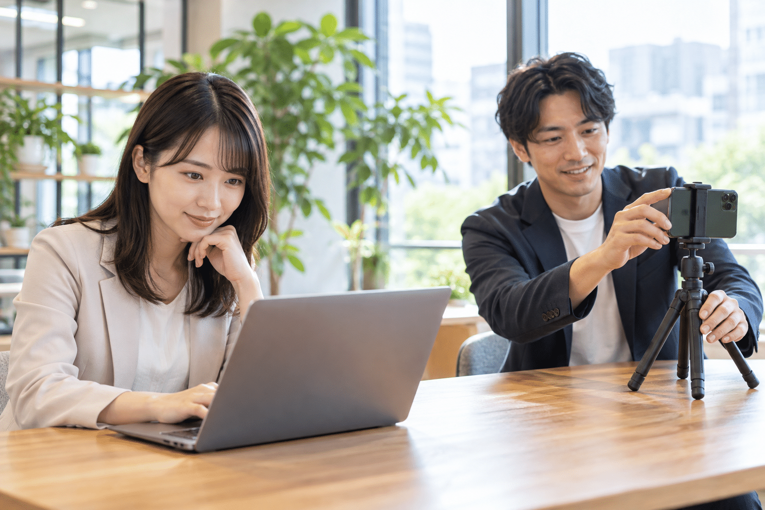 ノートPCで研修動画を見る女性と、スマートフォンで撮影準備をする男性
