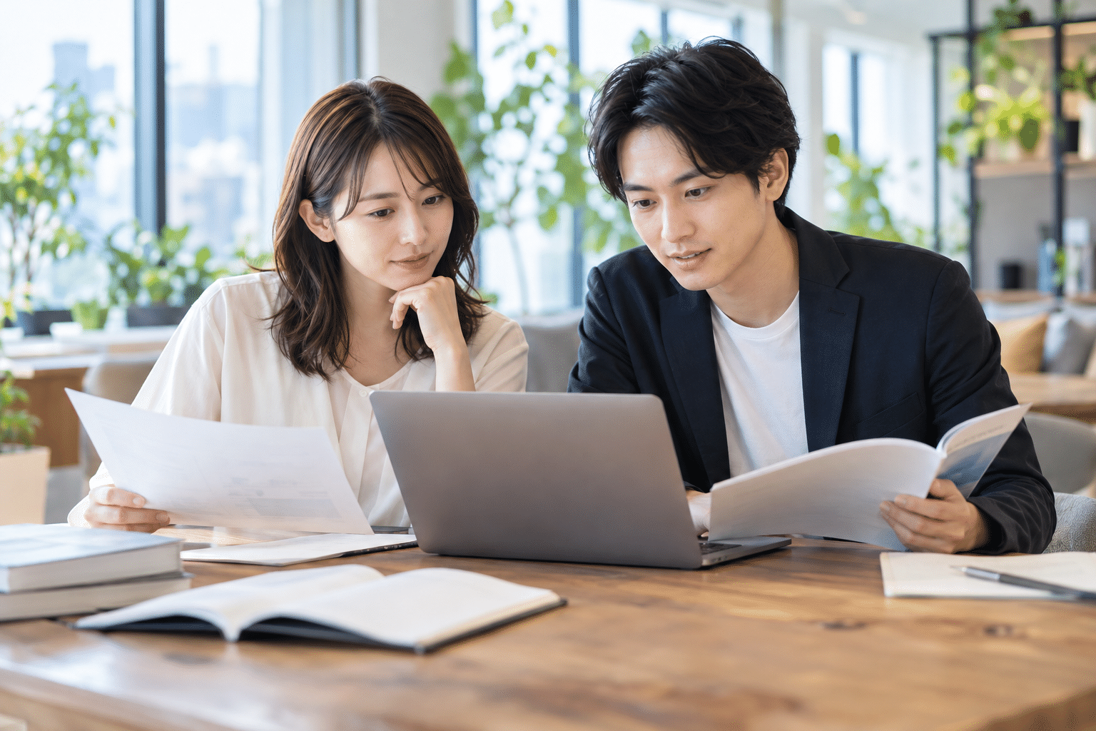 日本人の男女2人が木の机でノートPCを見ながら学習資料を読む
